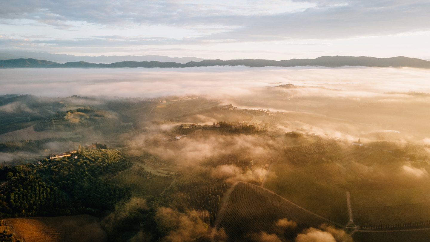 Vista aerea di colline nebbiose con vigneti e edifici.
