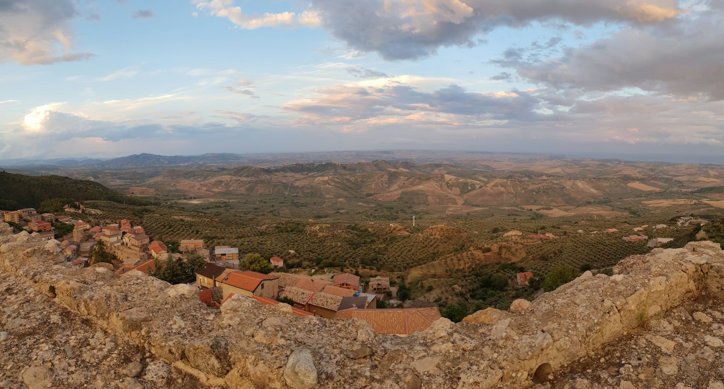 Colline ondulate con uliveti e tetti in terracotta vicino a un muro di pietra.