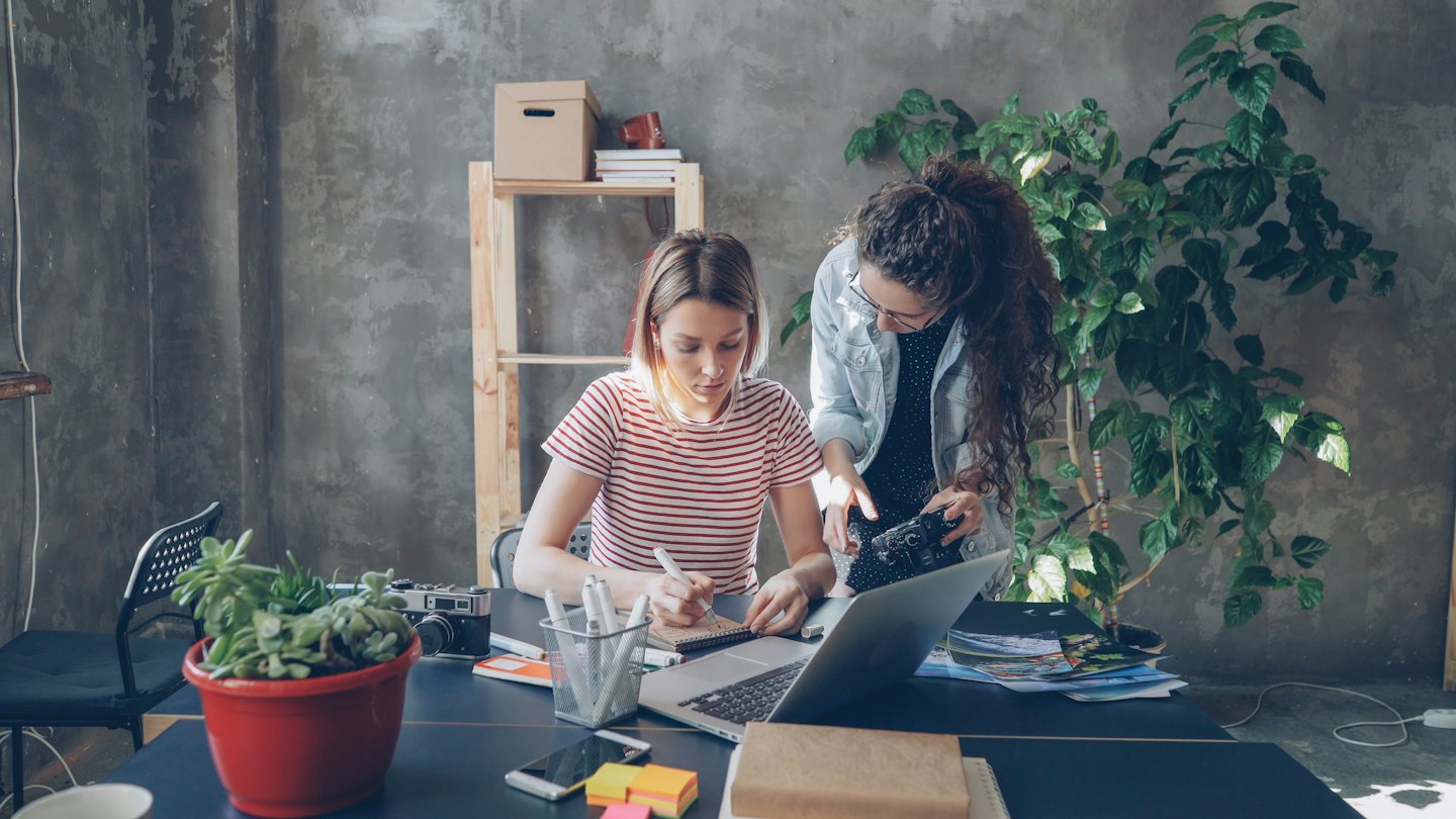 Due donne lavorano insieme a una scrivania con un laptop e una fotocamera.