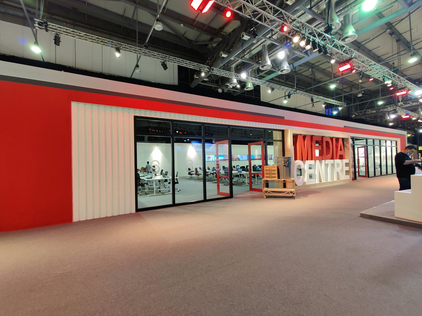 Persone lavorano all'interno di uno stand espositivo in un moderno centro multimediale.